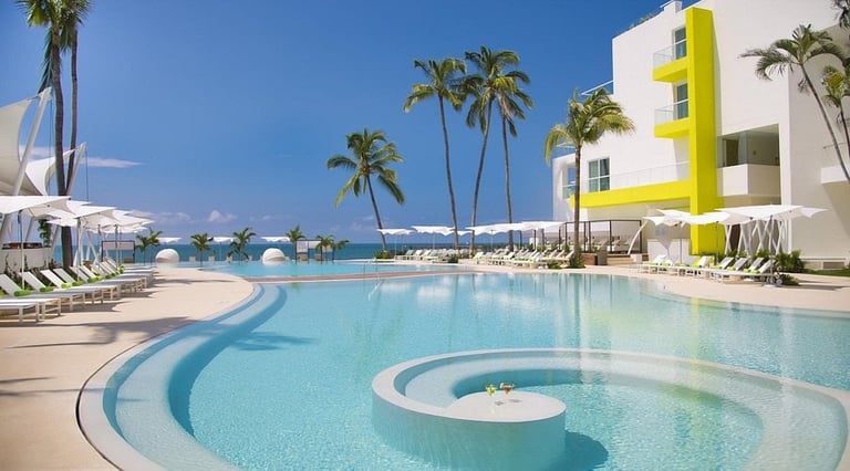 Luxury resort pool with curved design, white loungers, palm trees, and modern yellow-trimmed white building overlooking ocean.