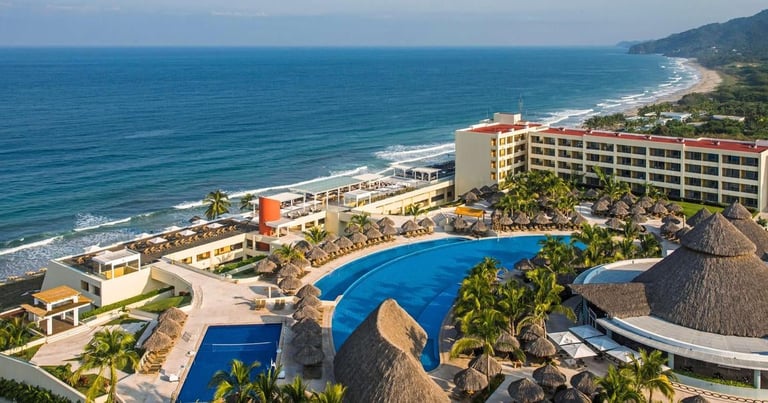 Beachfront resort with blue pool, palm trees, and ocean view with sandy beach and coastal hills