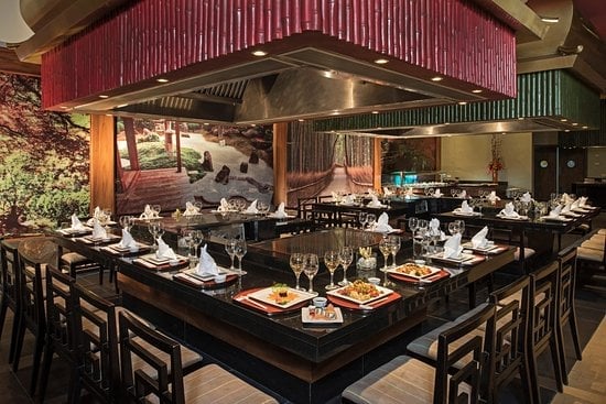 Modern open kitchen restaurant with red and green metal roof, black dining tables, plated dishes, and wine glasses.