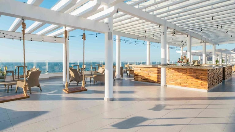 Modern rooftop lounge with white pergola, wooden bar counter, lounge chairs, and panoramic ocean views