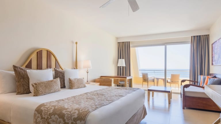 Modern hotel bedroom with king bed, ocean view windows, and contemporary furnishings